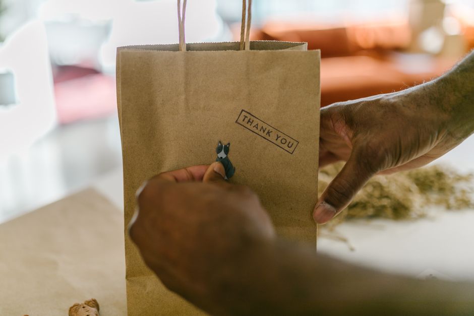 Un homme ajoute une étiquette "Thank You" sur un sac en papier brun, préparant un cadeau de dernière minute.