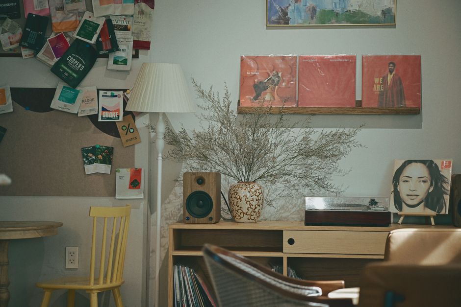 Coin cosy avec des vinyles, une plante décorative, une lampe et des affiches murales. Ambiance chaleureuse et artistique.