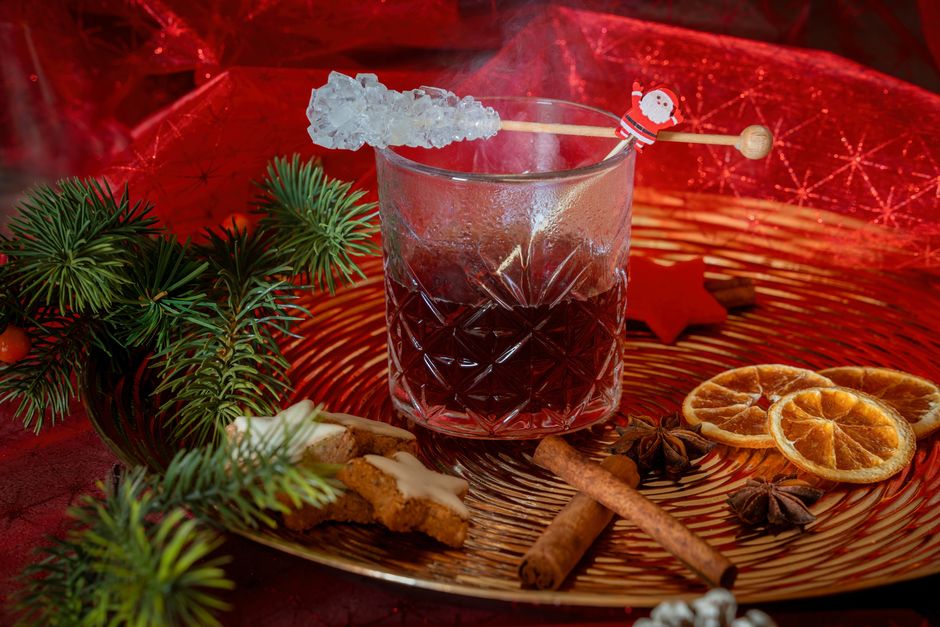 Verre de cocktail fumant décoré de glace, bâtons de cannelle et tranches d'orange sur un plateau doré, ambiance festive.