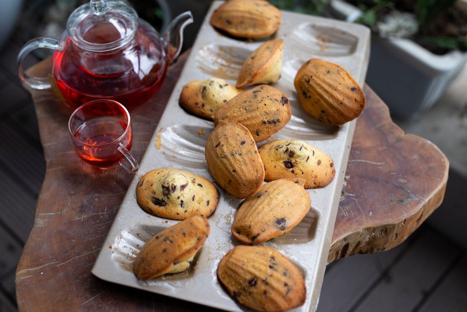 Plateau de madeleines dorées avec un verre de thé rouge à côté, sur une table en bois.
