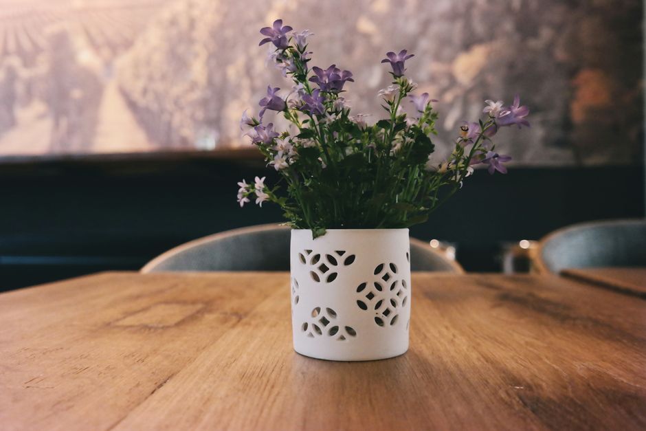 Vase blanc décoratif avec des fleurs violettes sur une table en bois, idéal pour une décoration de fête.