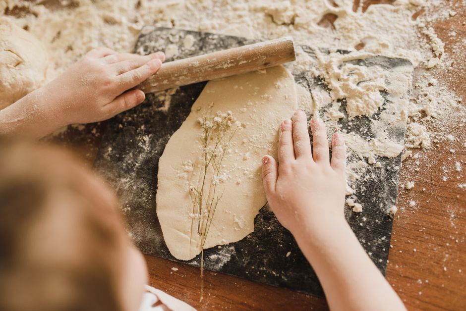 Enfant étalant de la pâte sur un plan de travail recouvert de farine, avec des fleurs séchées intégrées.