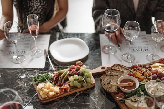 Table dressée avec des verres de vin, assiette vide et planche de fromages, fruits et pain, ambiance de dégustation.