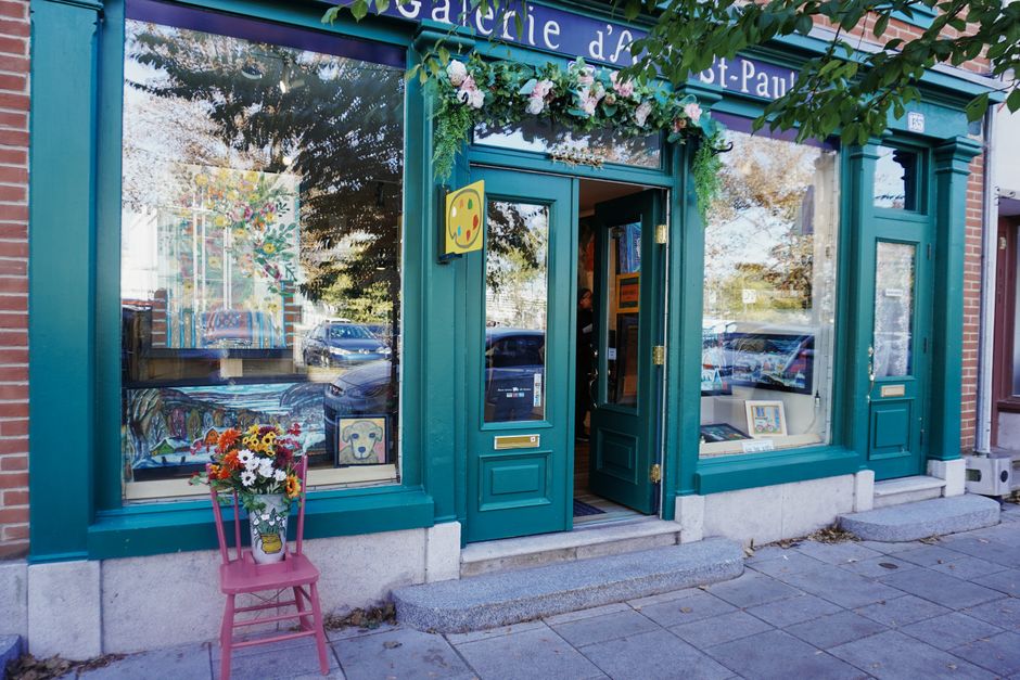 Boutique colorée avec des fleurs à l'entrée, exposant des créations artistiques à travers ses grandes fenêtres.