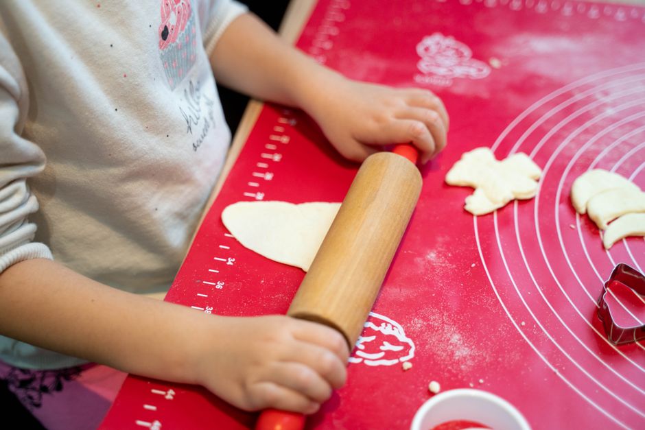 Enfant utilisant un rouleau à pâtisserie pour étaler de la pâte sur un plan de travail rouge, avec des emporte-pièces à proxi