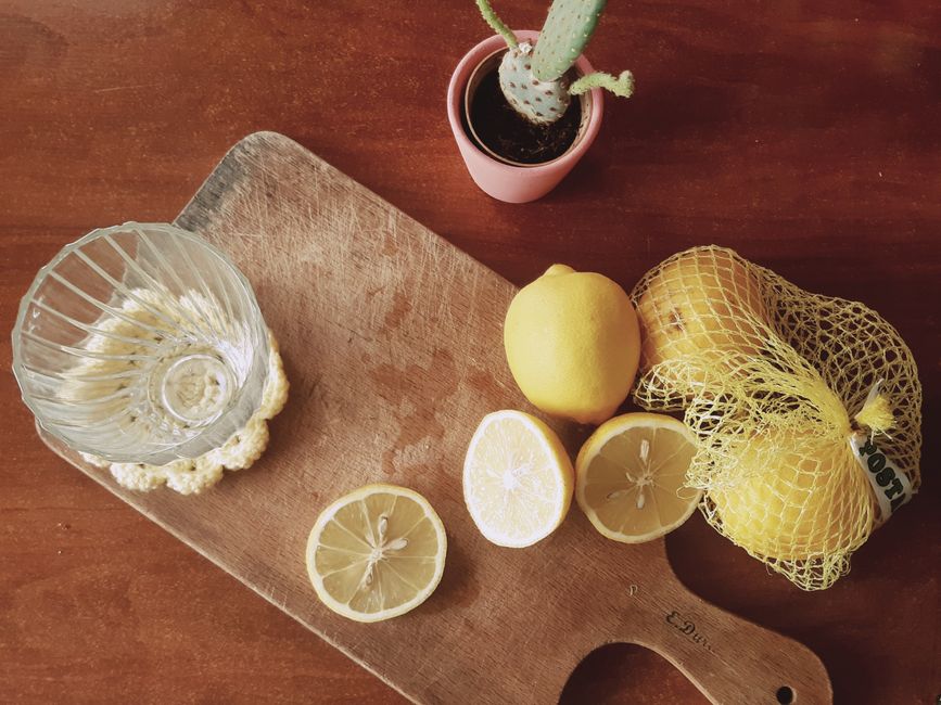 Planche en bois avec des citrons, un verre vide et un petit cactus en pot sur une table en bois.