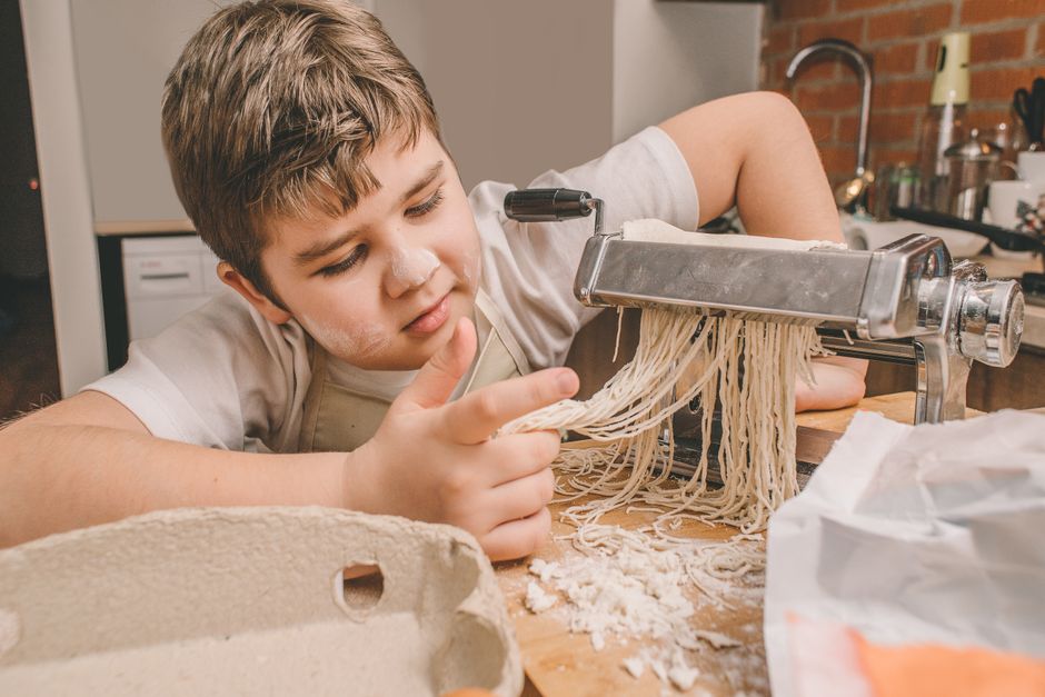 Un enfant utilise une machine à pâtes pour préparer des nouilles maison dans une cuisine chaleureuse.