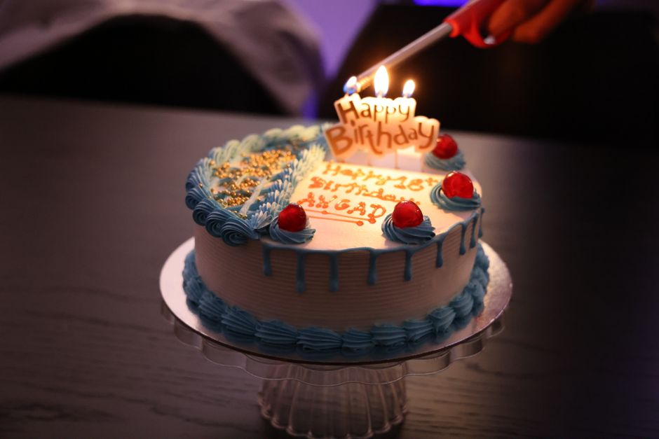 Gâteau d'anniversaire décoré avec des bougies et des fruits, sur une table sombre, prêt à être célébré.