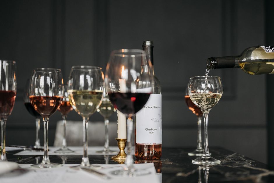 Verres de vin de différentes couleurs sur une table élégante, une bouteille de vin blanc est versée dans un verre.
