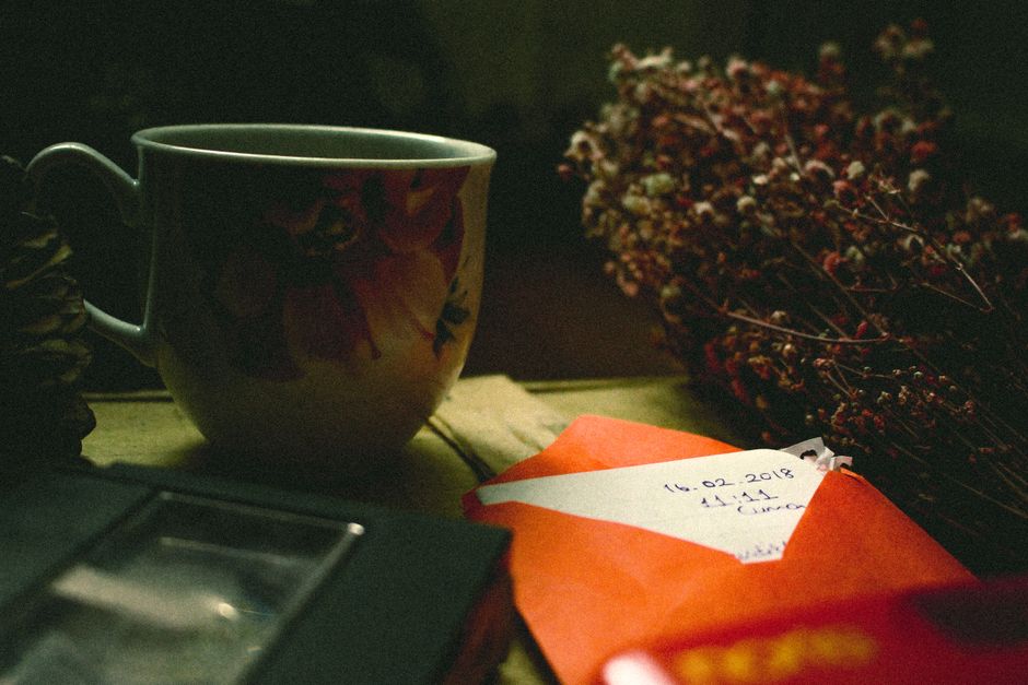 Tasse décorée, enveloppe rouge et fleurs séchées sur une table en bois, évoquant des attentions pour dire merci.