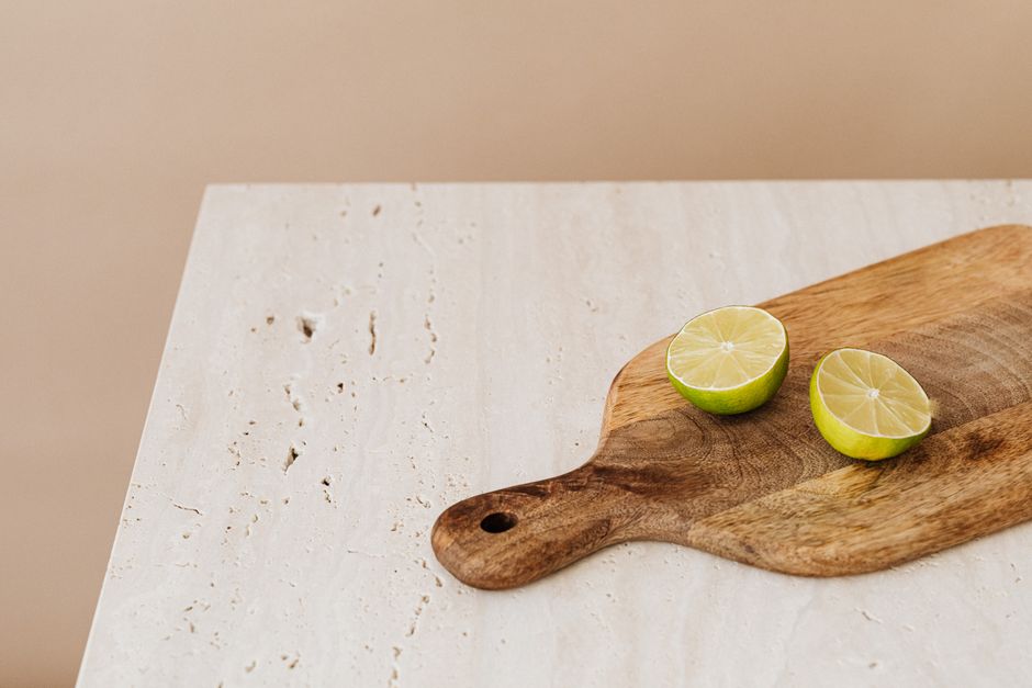 Deux moitiés de citron vert sur une planche en bois, posées sur une table en marbre clair.