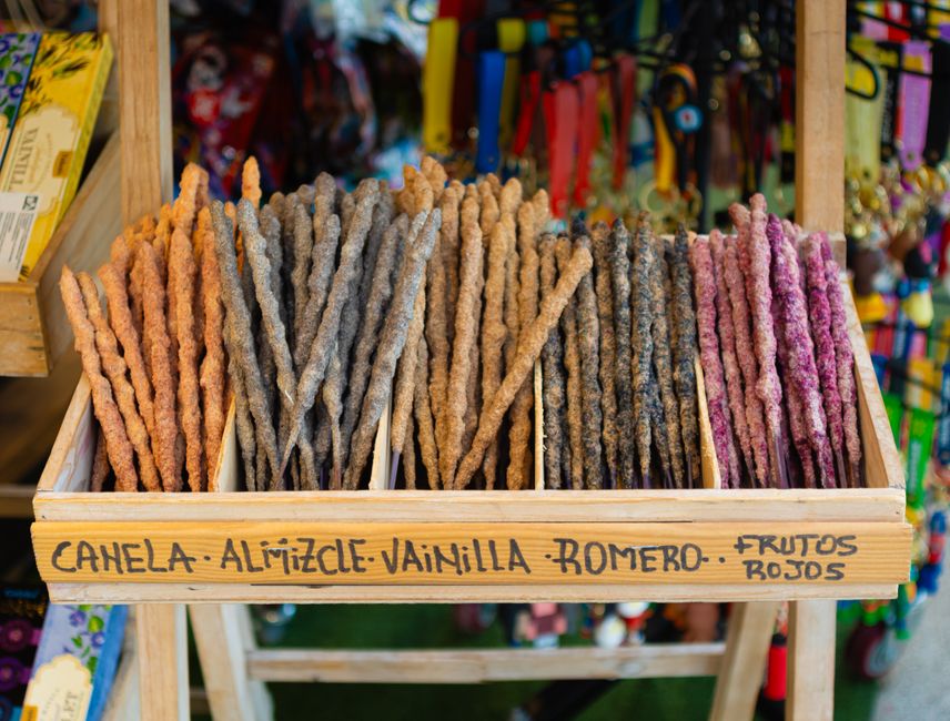 Étagère en bois avec des bâtons de cannelle, vanille et cardamome colorés, présentés dans un marché.