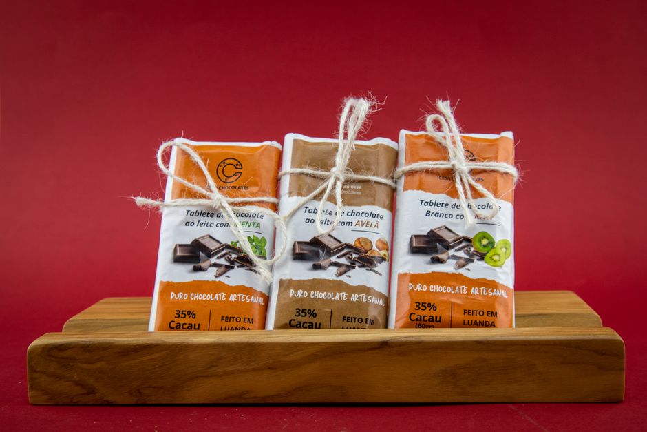 Trois tablettes de chocolat sur un support en bois, avec emballages colorés sur fond rouge.