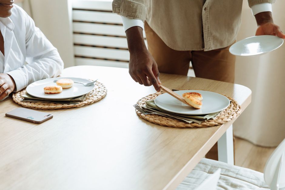 Un homme place des assiettes sur une table en bois avec des sets de table en osier, préparant un repas convivial.