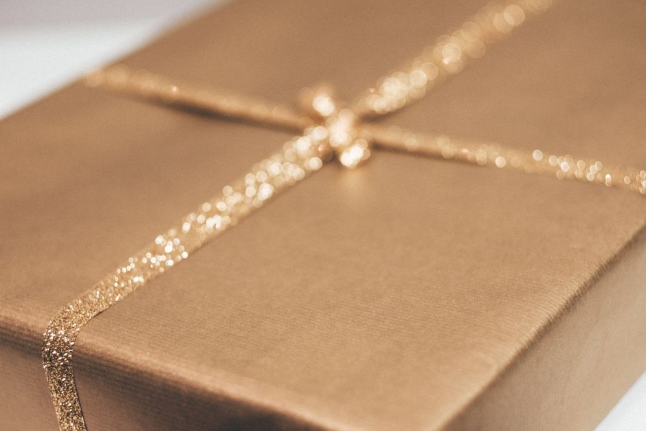 Cadeau emballé dans un papier doré avec un ruban scintillant, symbolisant l'idée de cadeaux sensoriels.