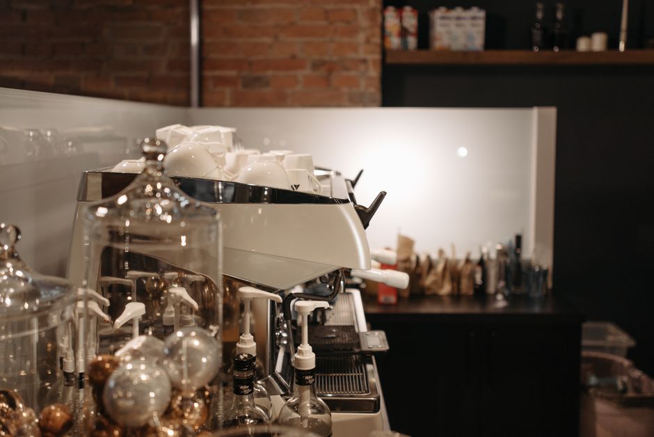 Machine à café moderne avec tasses blanches et décor en briques, ambiance chaleureuse d'un café urbain.