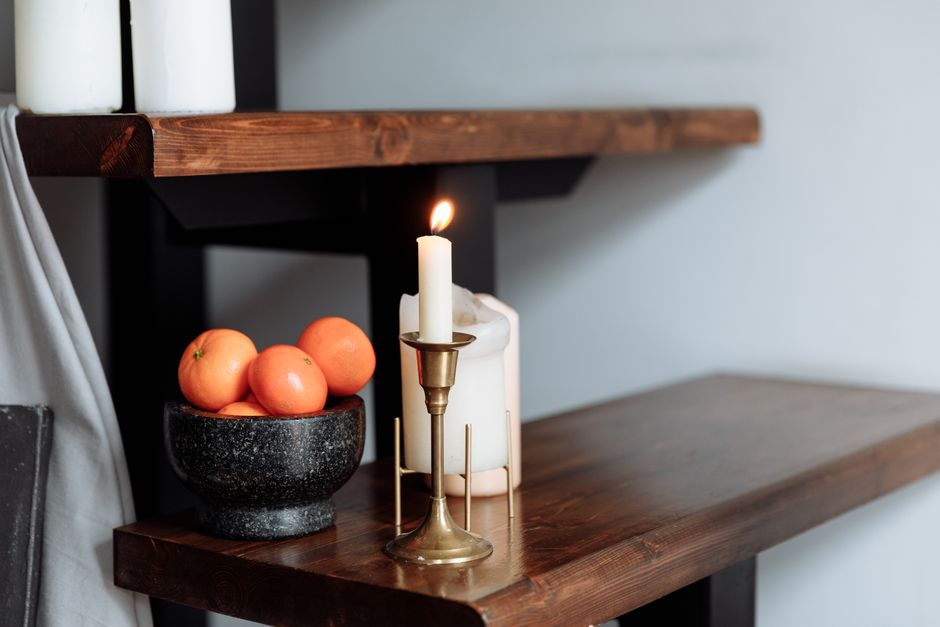 Bougie allumée et fruits dans un bol sur une étagère en bois, évoquant une ambiance chaleureuse et nostalgique.