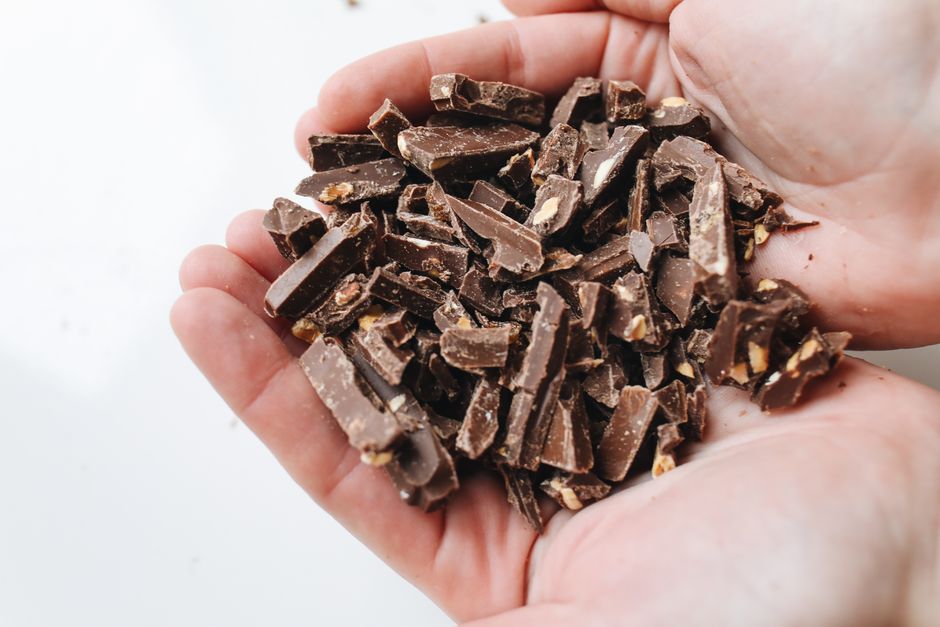 Mains ouvertes tenant des morceaux de chocolat noir, symbolisant réconfort et plaisir gourmand.