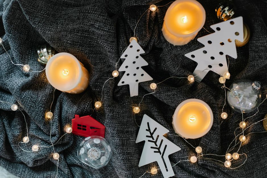 Bougies allumées, décorations de Noël et guirlande lumineuse sur un plaid gris, créant une ambiance apaisante.