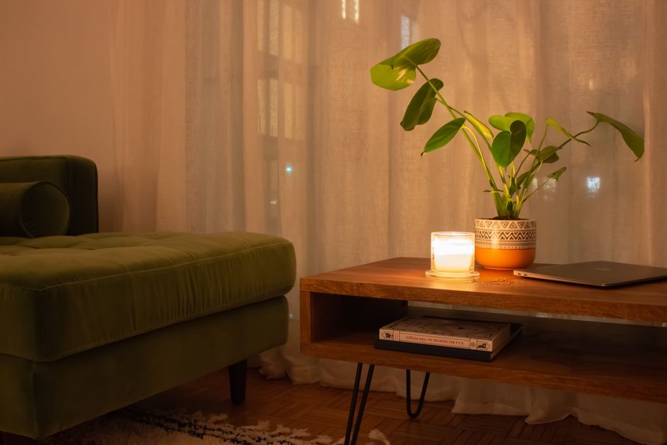 Coin détente avec un canapé vert, une table en bois, une bougie allumée et une plante verte, créant une ambiance apaisante.