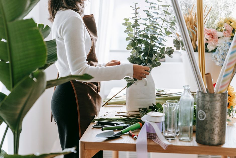 Fleuriste préparant un bouquet avec des branches d'eucalyptus sur une table de travail bien organisée.