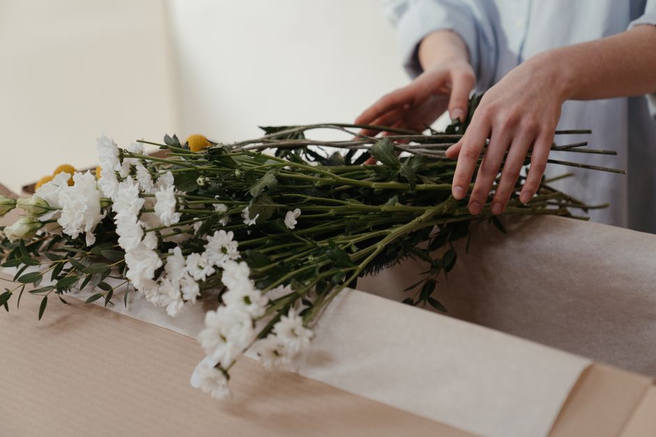 Fleuriste préparant un bouquet avec des fleurs blanches et des feuillages dans une boîte en carton.