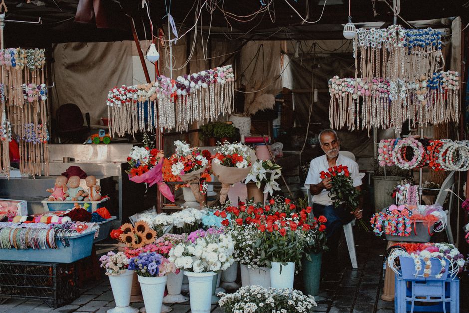Un vendeur de fleurs arrange des bouquets colorés dans un marché aux fleurs animé, entouré de décorations florales.