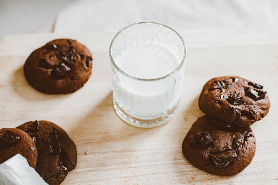 Biscuits au chocolat accompagnés d'un verre de lait sur une planche en bois, parfaits pour un goûter en famille.