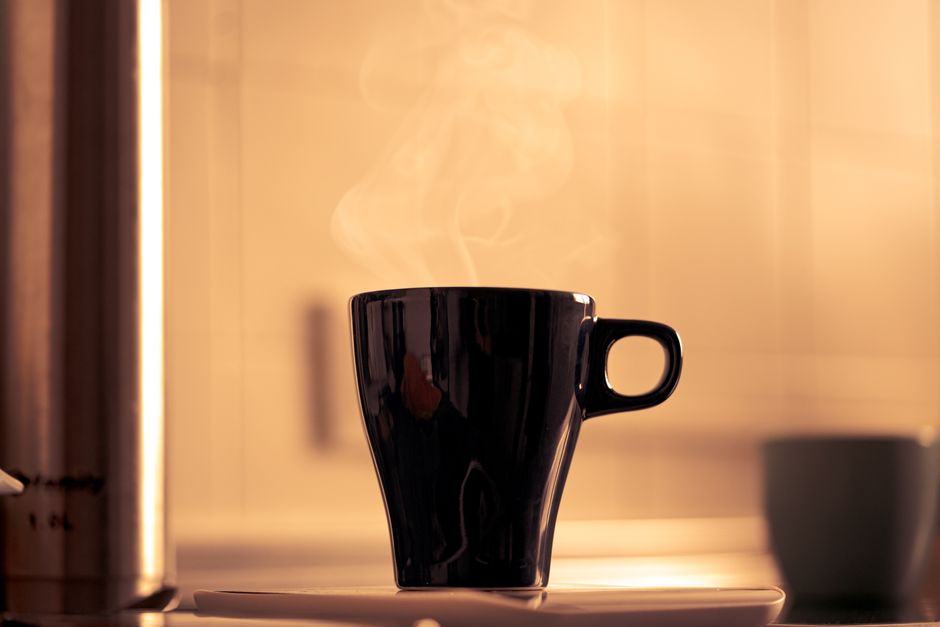 Tasse de café fumant sur une soucoupe, éclairage doux et ambiance chaleureuse.