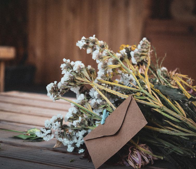 Bouquet de fleurs séchées avec une enveloppe en papier kraft sur une table en bois, symbole de remerciement.