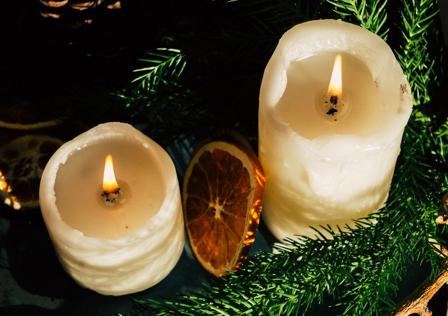 Bougies allumées entourées de branches de sapin et d'orange séchée, évoquant des souvenirs olfactifs.