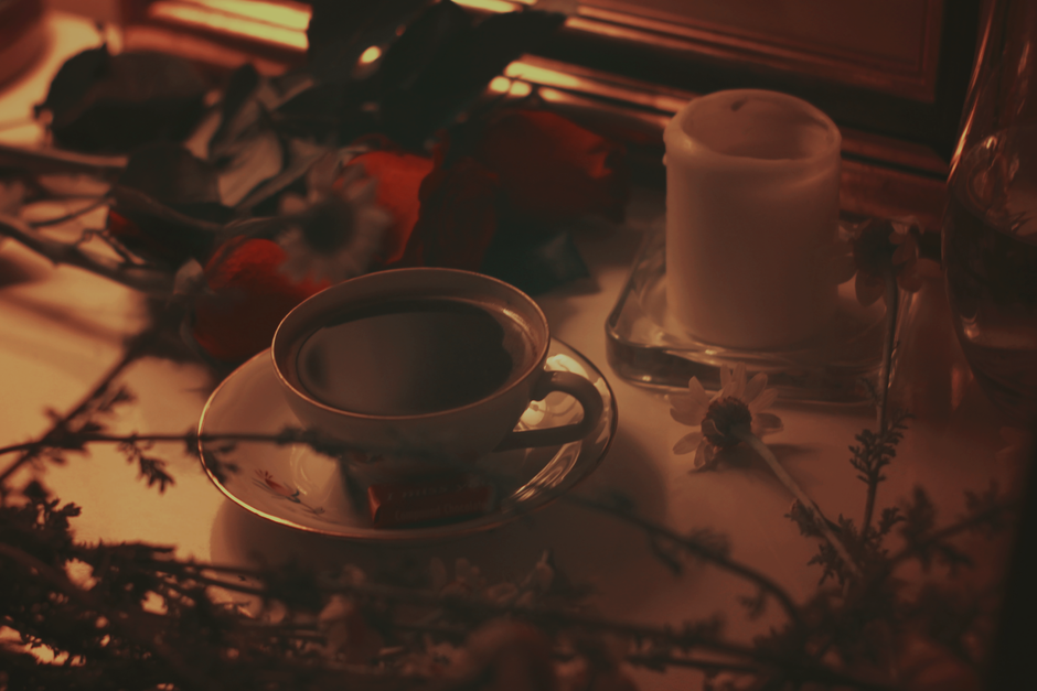 Tasse de café noir posée sur une table décorée de fleurs et d'une bougie, créant une ambiance chaleureuse.