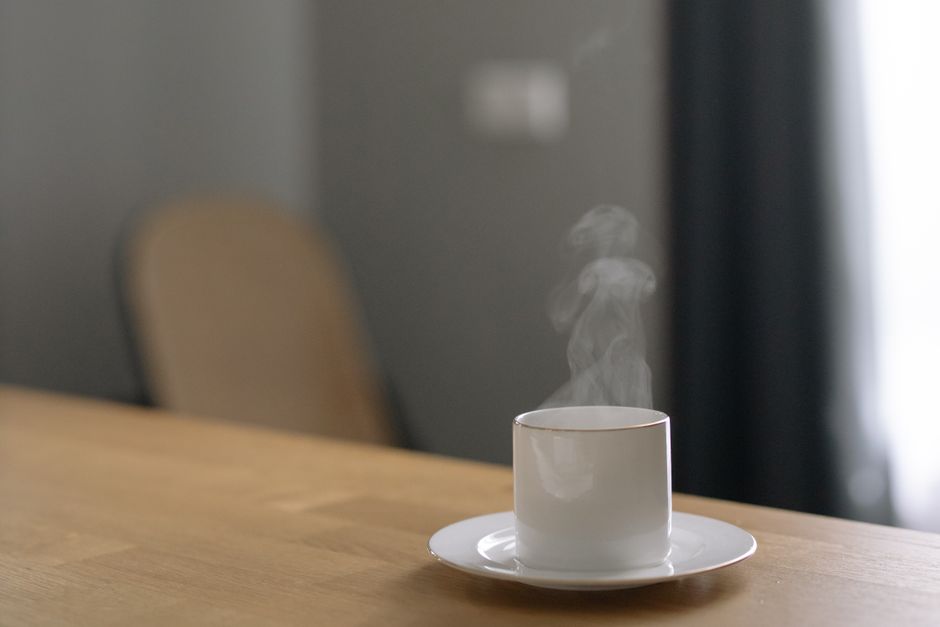 Tasse blanche fumante sur une table en bois, évoquant un moment de détente avec une boisson chaude.
