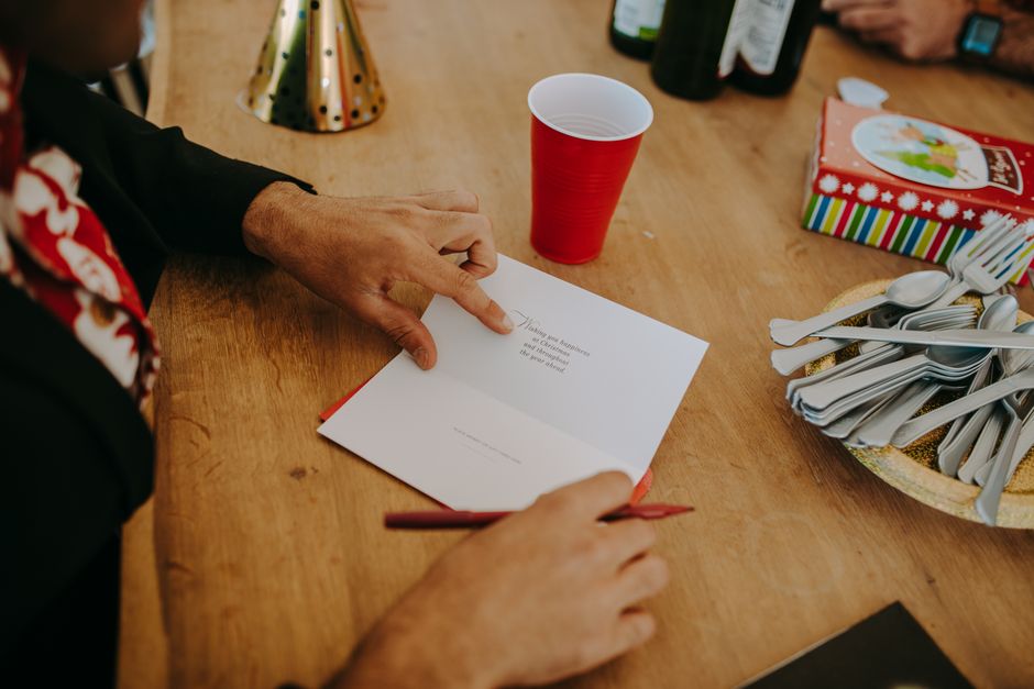 Personne écrivant un message dans une carte de vœux sur une table avec des couverts et un gobelet rouge.
