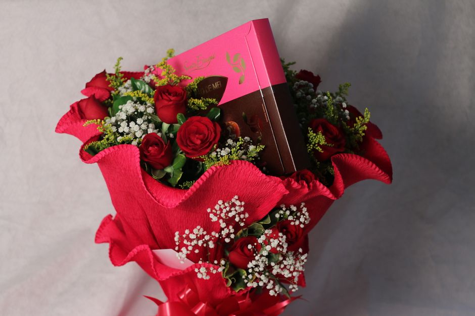 Bouquet de roses rouges entouré de fleurs blanches et d'une boîte de chocolat rose. Idéal pour un cadeau romantique.