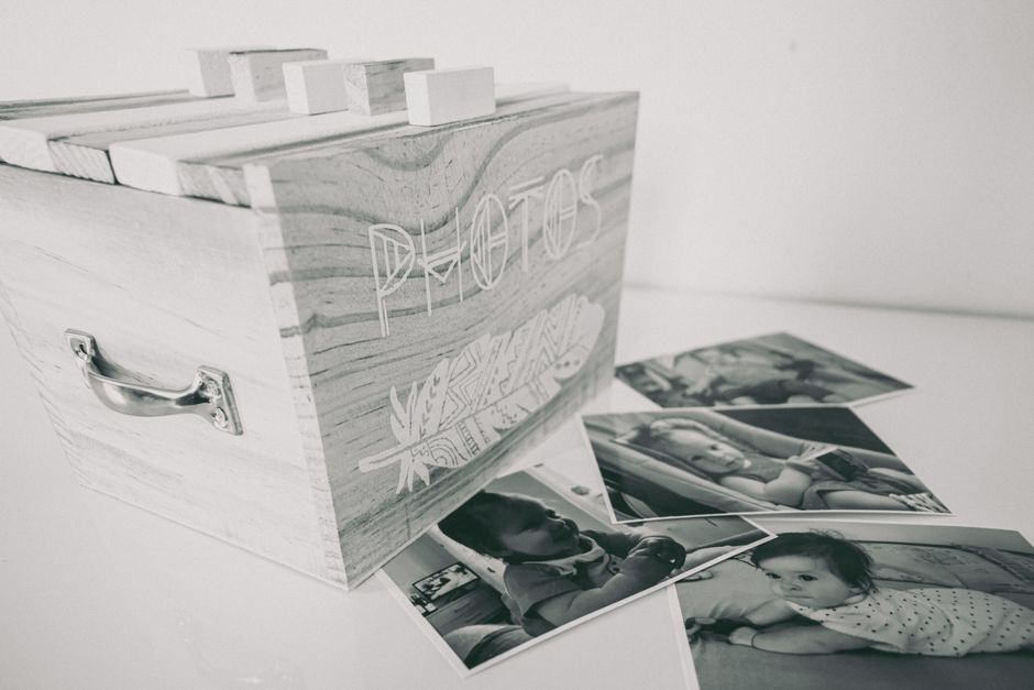 Boîte à souvenirs en bois avec le mot "PHOTOS" gravé, entourée de photos en noir et blanc d'enfants.