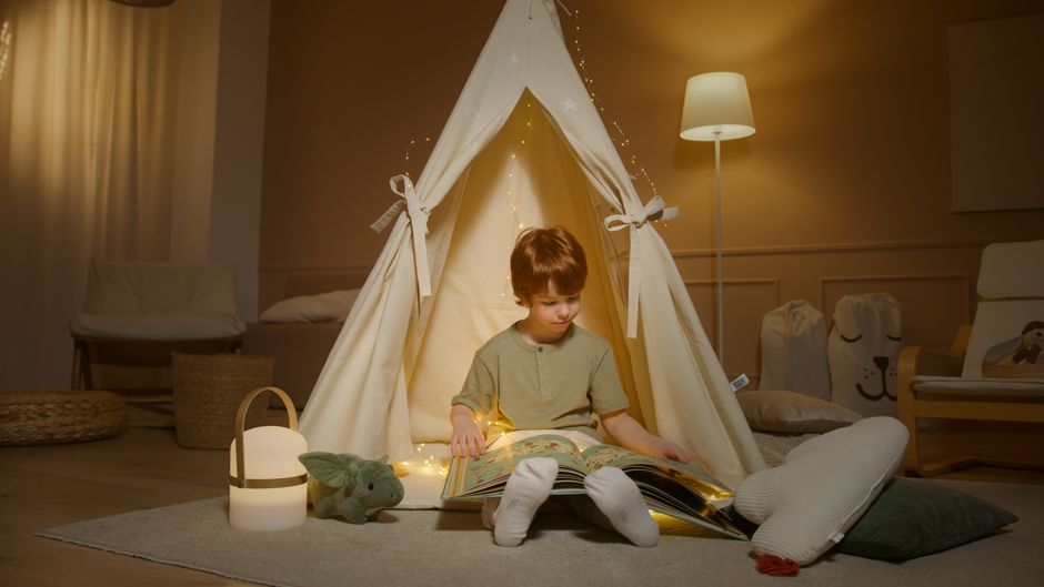 Enfant assis dans une tente de jeu, lisant un livre avec des lumières douces autour, créant une ambiance apaisante.