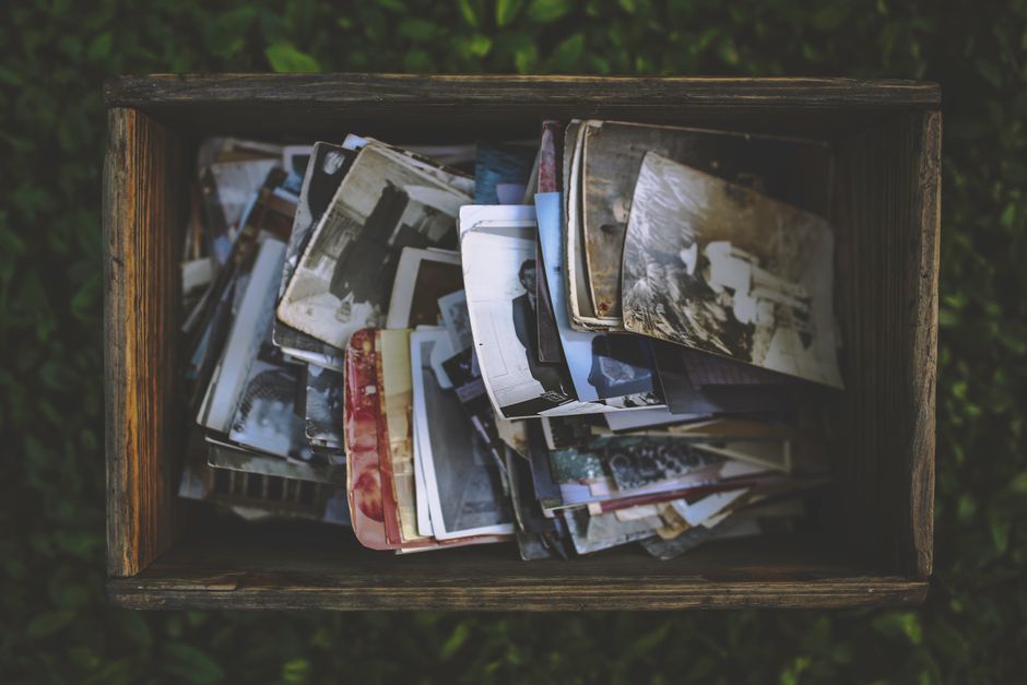 Boîte en bois remplie de vieilles photos en noir et blanc sur un fond de verdure.