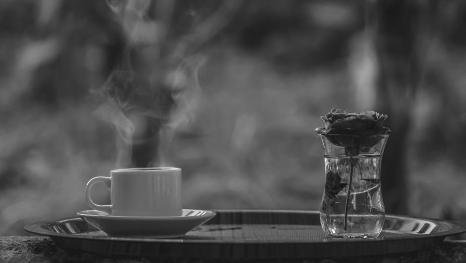 Tasse de thé fumant à côté d'un vase transparent avec une rose, sur un plateau en bois.