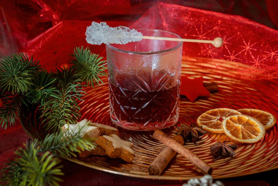Verre de boisson chaude avec glaçon, bâtons de cannelle, étoiles de badiane et tranches d'orange sur un plateau doré.