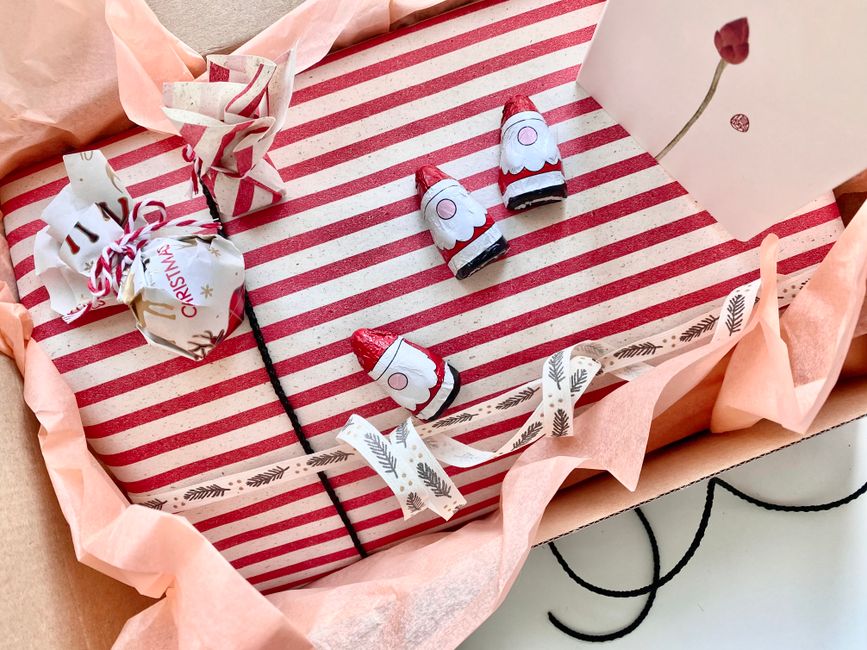 Cadeau joliment emballé avec du papier rayé, décoré de petits gnomes et d'une carte, évoquant une surprise festive.