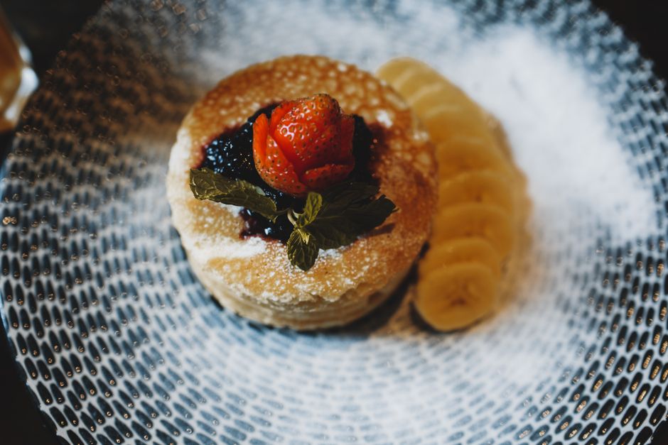 Pancakes garnis de fruits rouges et de banane, servis sur une assiette élégante, parfaits pour un brunch.