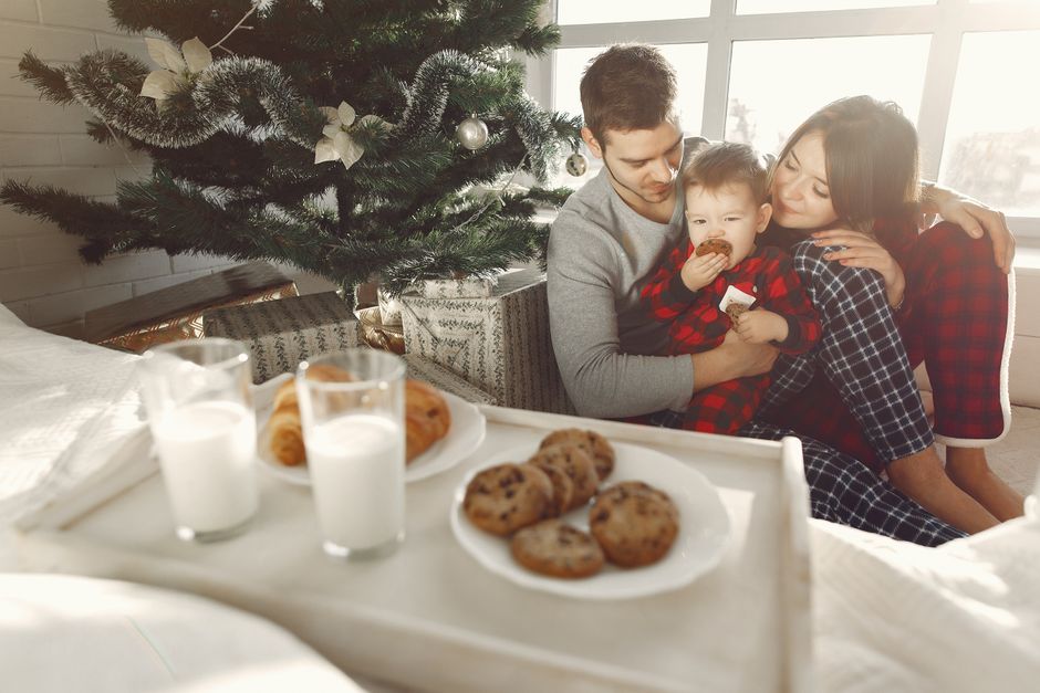 Famille réunie autour d'un goûter avec biscuits et lait, assise près d'un sapin de Noël.