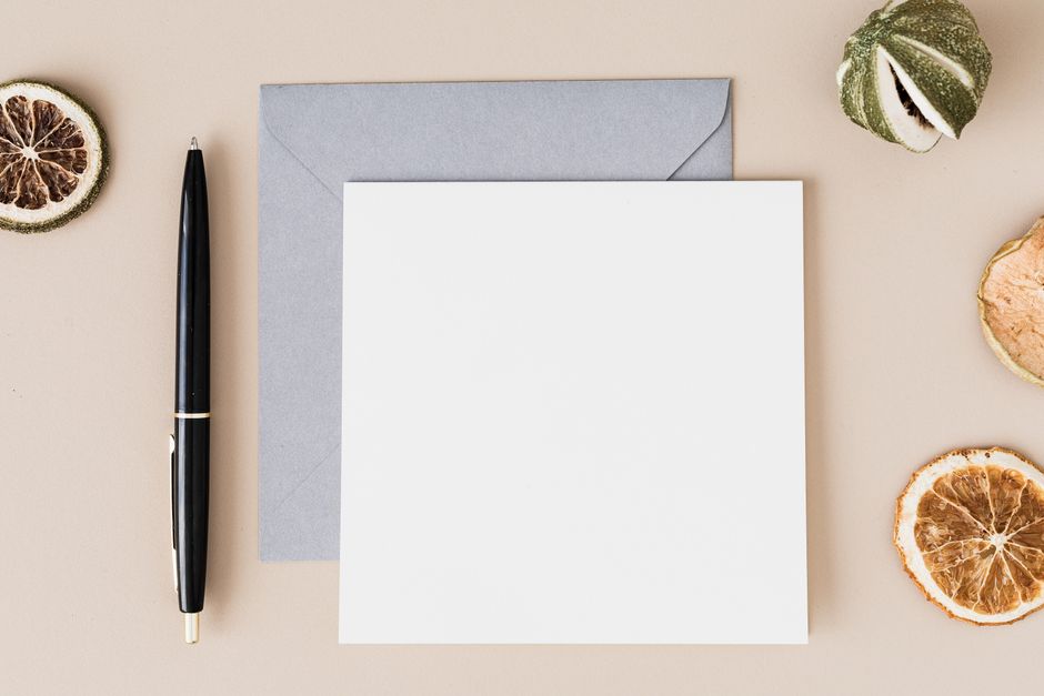 Carte blanche avec une enveloppe grise et un stylo noir, entourée de tranches d'agrumes séchées.