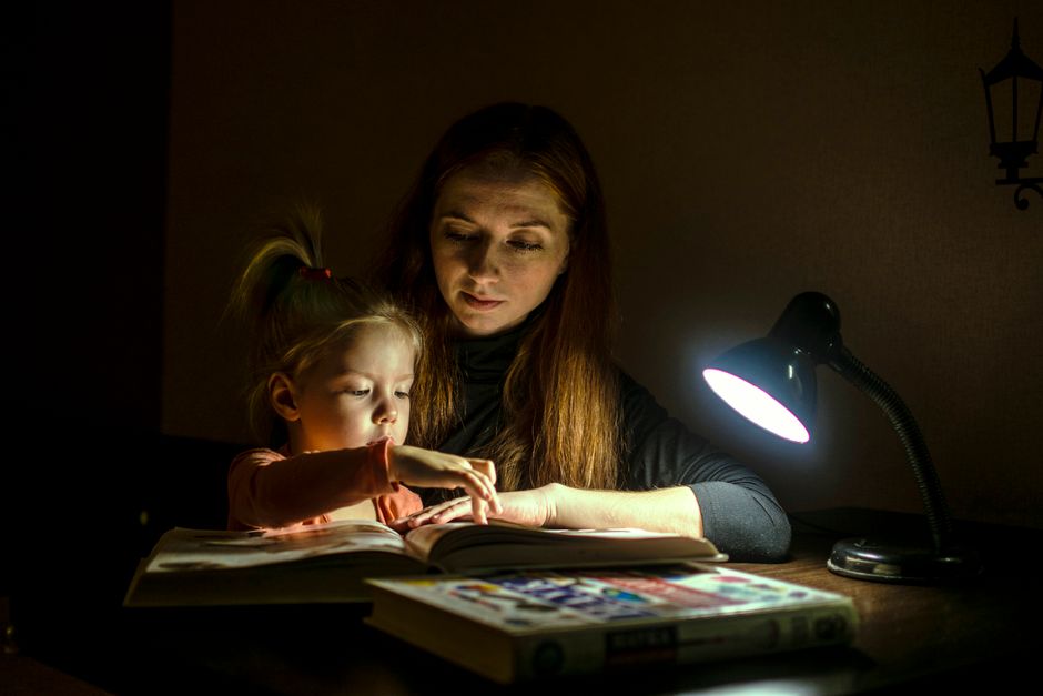 Mère lisant un livre à sa fille sous une lampe de bureau, créant un moment apaisant avant le coucher.