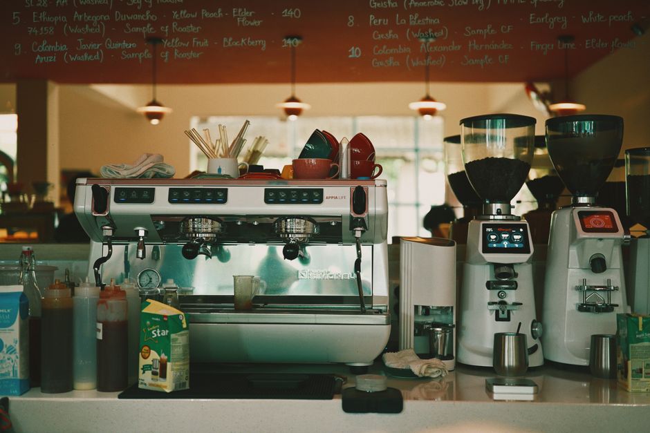 Machine à café moderne avec tasses colorées, sirops et moulin à café, dans un café lumineux et accueillant.
