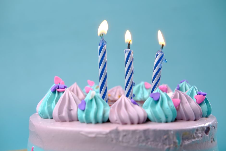 Gâteau d'anniversaire décoré de crème pastel avec trois bougies allumées et des confettis en forme de cœur.
