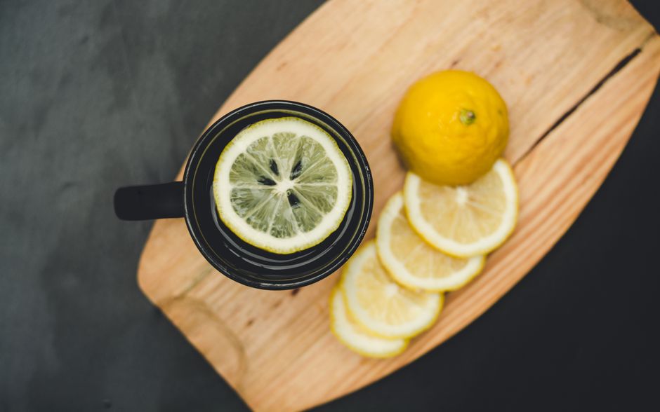 Tasse de thé au citron avec des rondelles de citron et un citron entier sur une planche en bois.